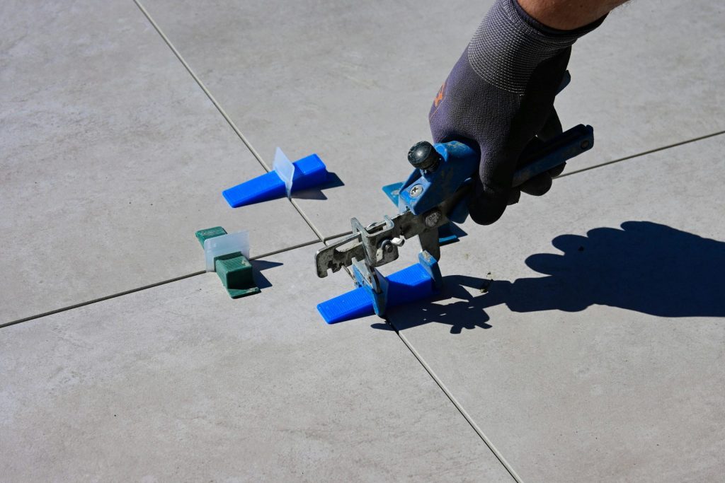 Une main gantée utilisant un outil de nivellement pour poser des carreaux à l'aide d'entretoises.